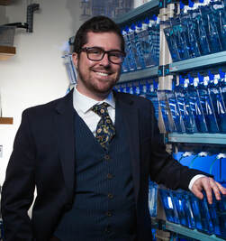 Portrait of smiling Beck Wehrle in a three piece suit with a lizard tie, zebrafish tanks in background